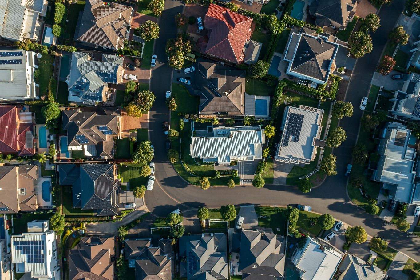 Aerial view of a suburban neighborhood showing a variety of houses with different roof types and small, green backyards.