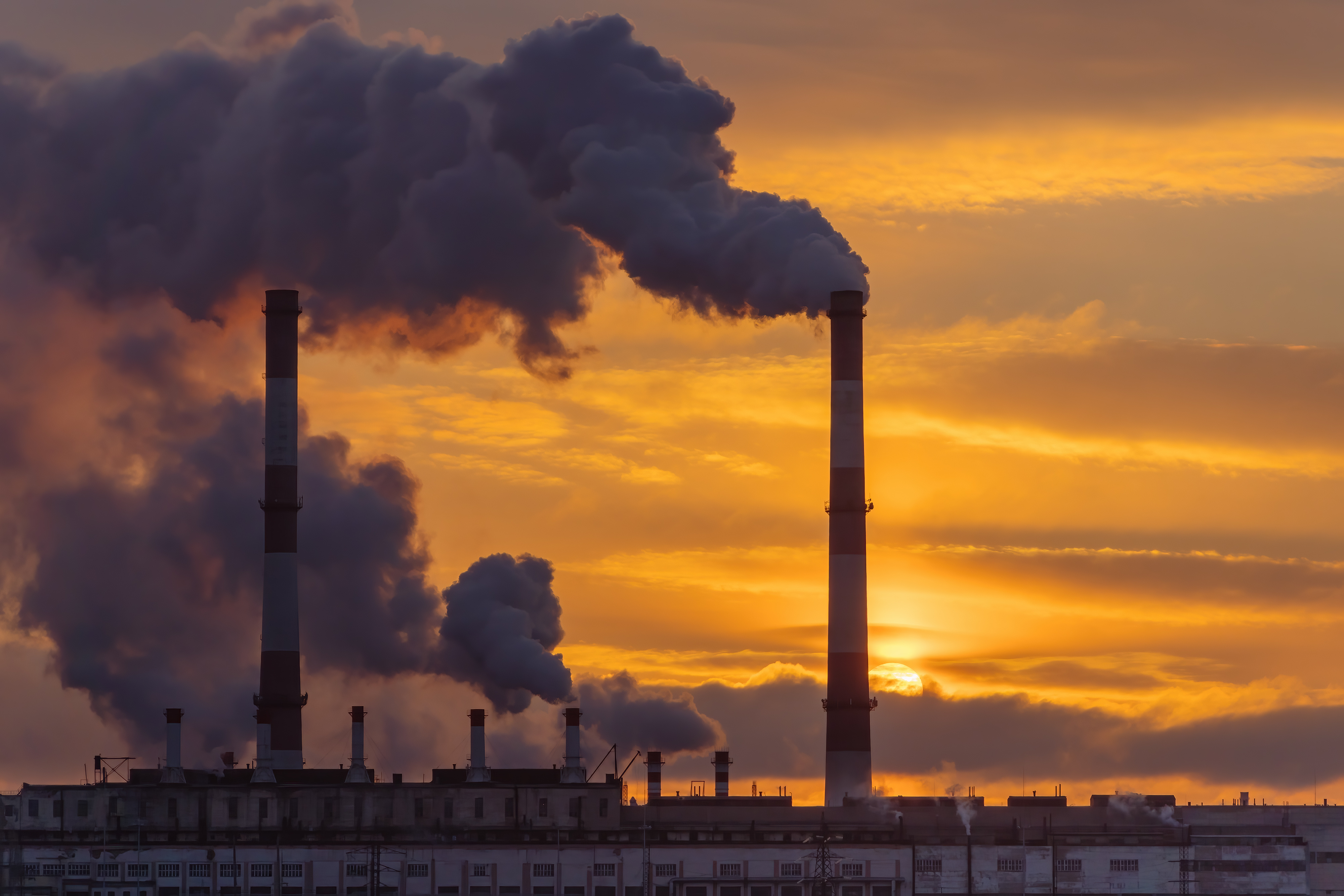 AdobeStock 487435409 Sunset behind industrial area with stack emitting pollutants