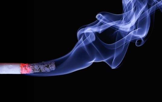 A lit cigarette with smoke swirling against a black background.