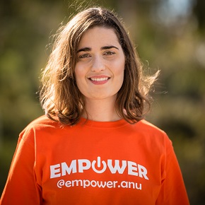 A woman smiling at the camera, wearing an orange t-shirt with the word "EMPOWER" and a handle "@empower.anu" printed on it.