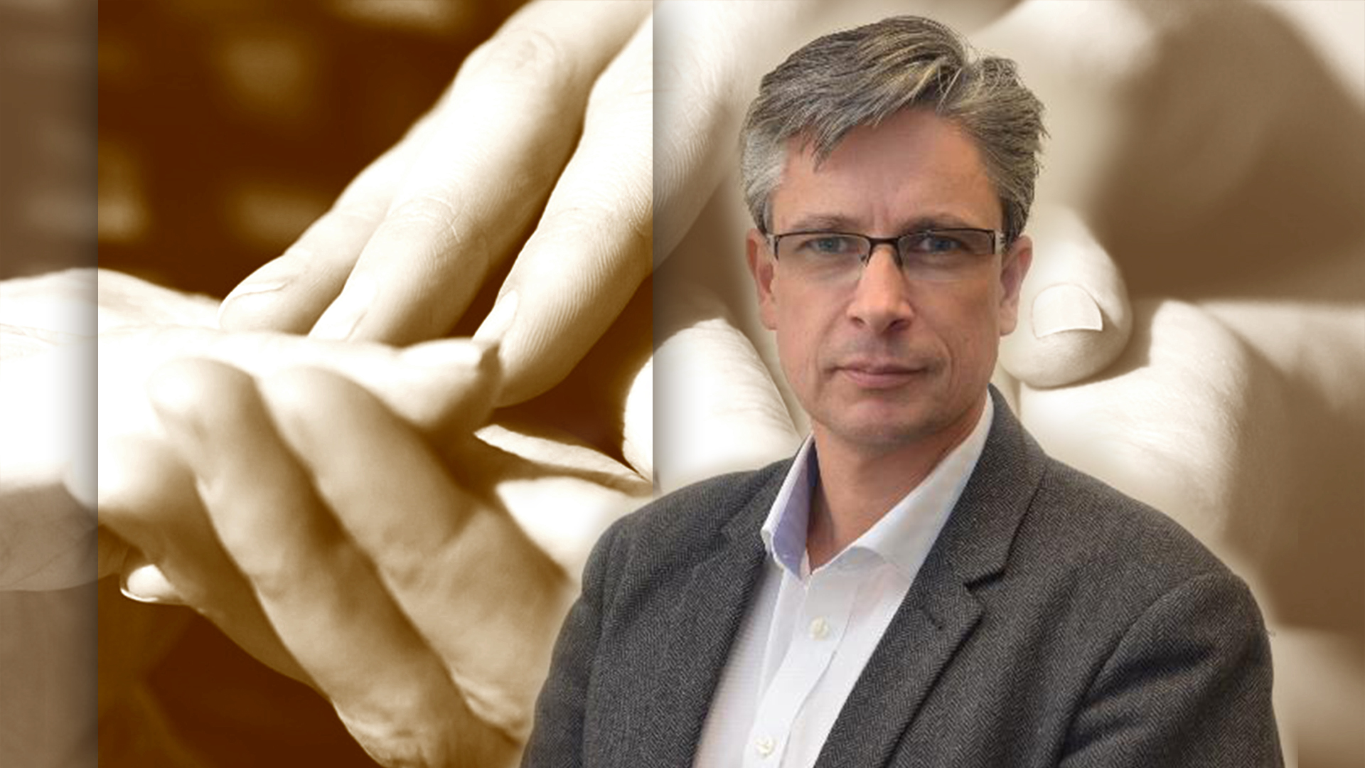 A man in glasses and a blazer stands in front of a blurred background, with a superimposed image of two hands almost touching, reminiscent of Michelangelo's "Creation of Adam."