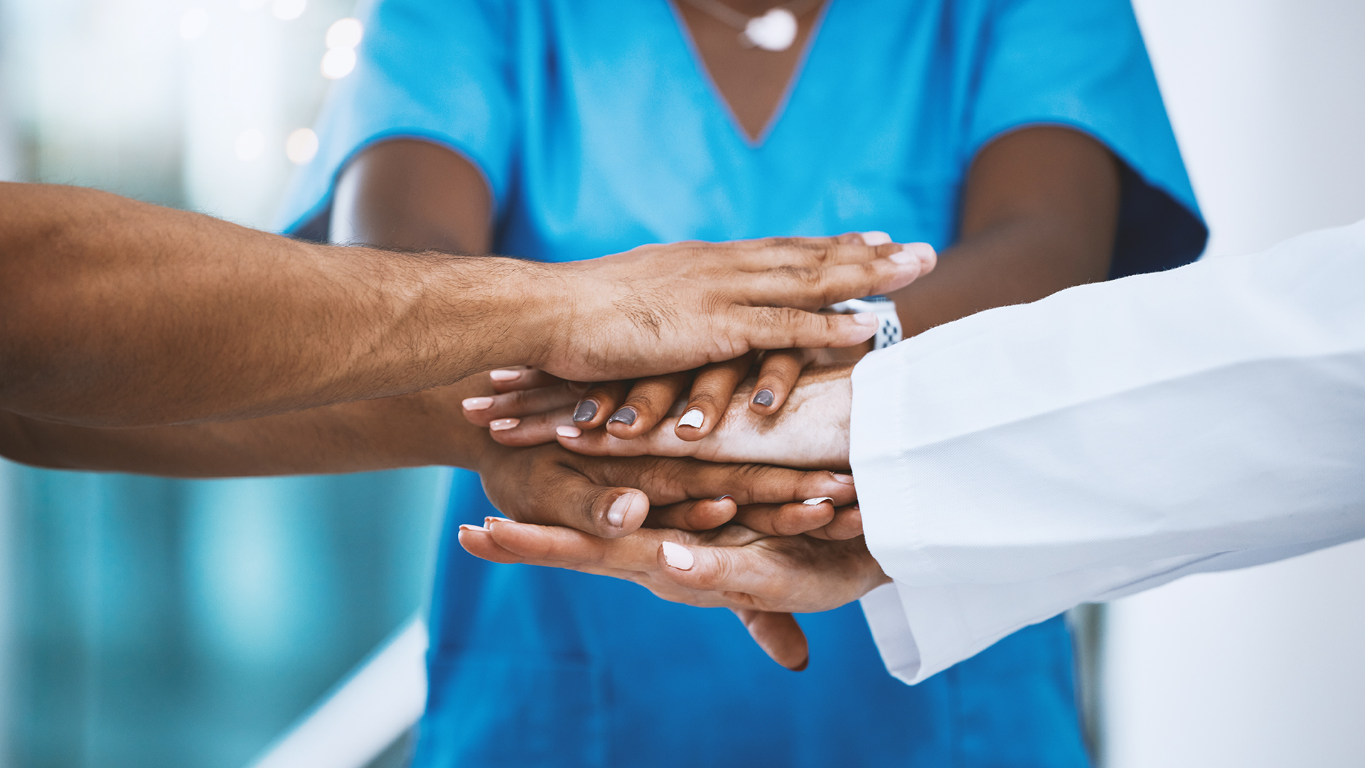 A group of healthcare workers stacking hands together in a gesture of teamwork and unity.