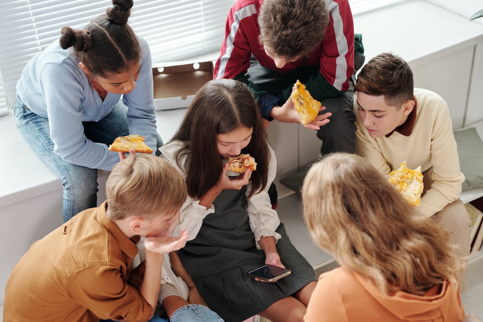 A group of teenagers enjoy eating pizza together in a casual, home setting.