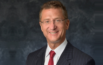 A professional portrait of a smiling man wearing a pinstripe suit and red tie.