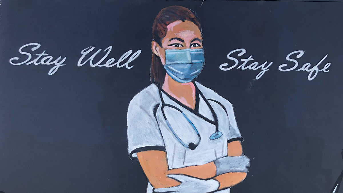 A mural of a nurse wearing a face mask with the words "Stay Well Stay Safe" written above and beside her.