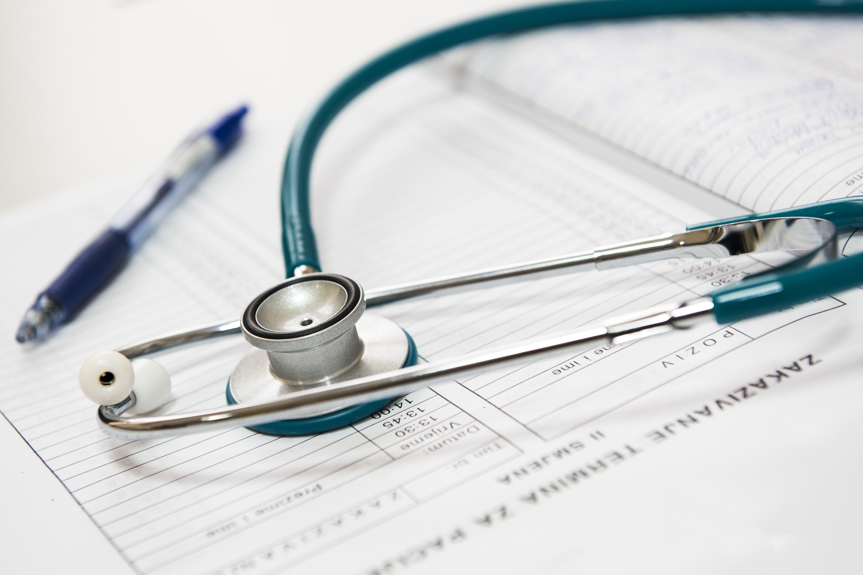 A stethoscope and a pen lying on an open medical chart, indicating a clinical setting.