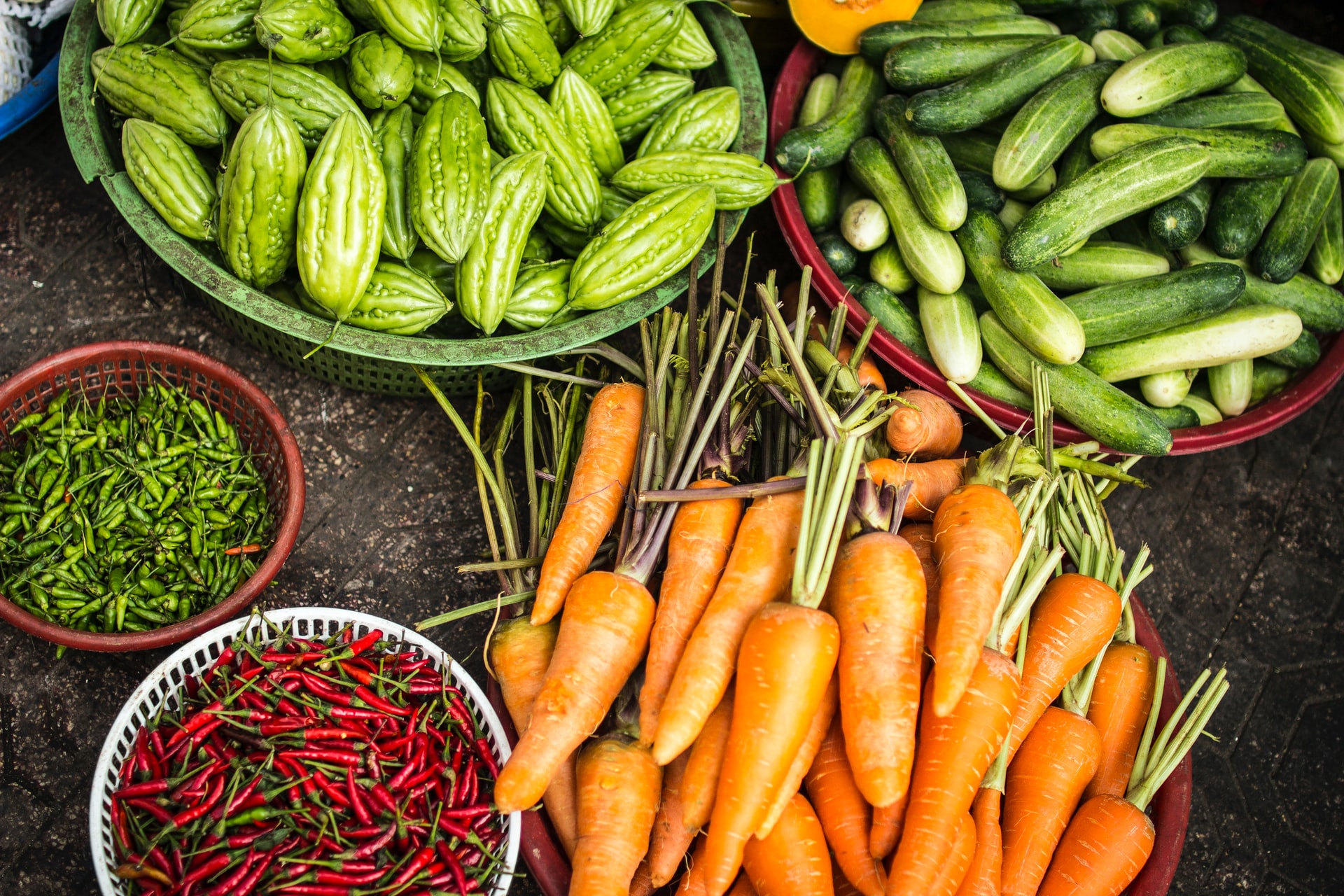 Various fresh vegetables including carrots, cucumbers, and chili peppers displayed in baskets at a market.