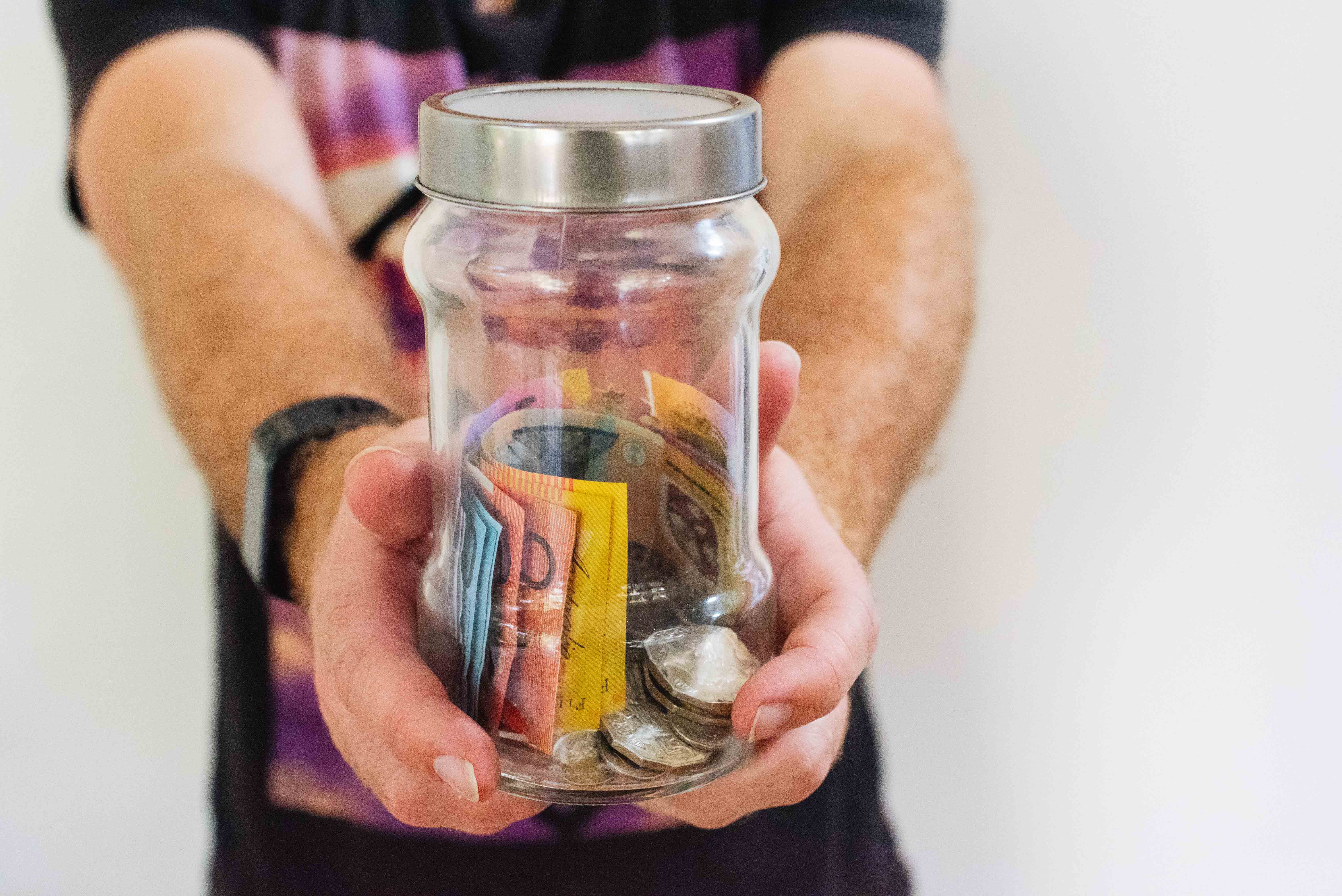 A person holding a glass jar filled with coins and banknotes.