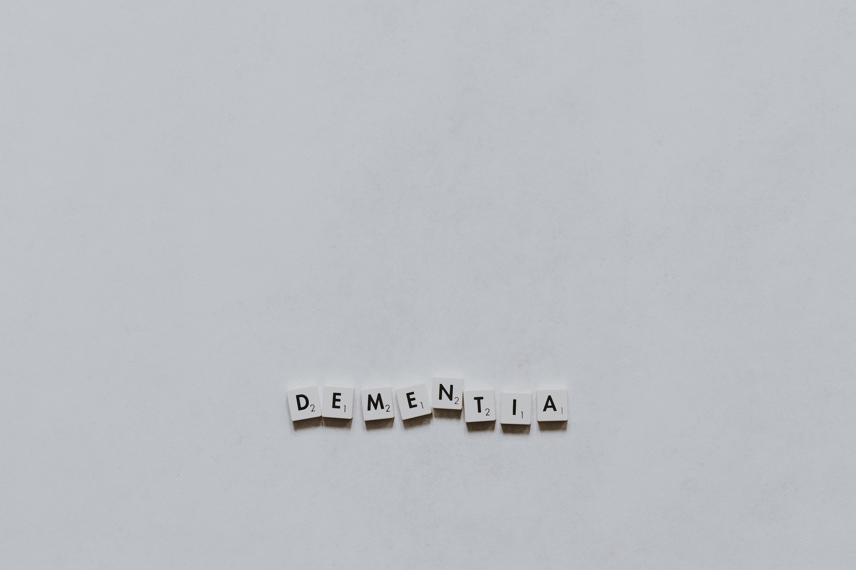 The word "DEMENTIA" spelled out in scrabble tiles on a plain white background.