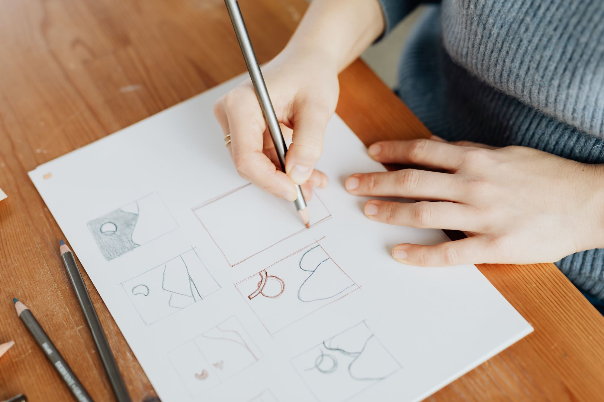 A person sketching various jewelry designs on a white paper.