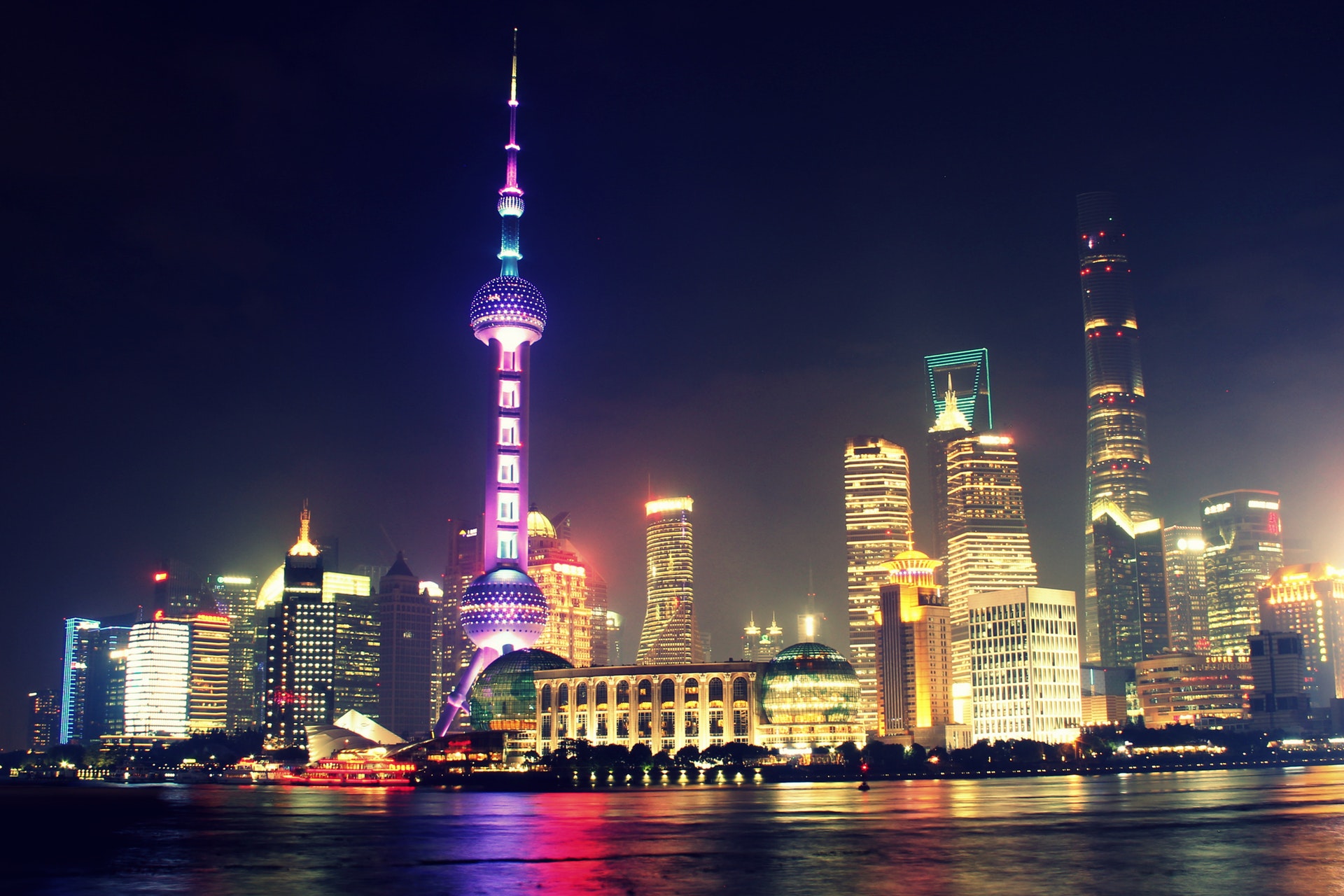 Night view of the illuminated Shanghai skyline featuring the Oriental Pearl Tower and modern high-rise buildings along the waterfront.