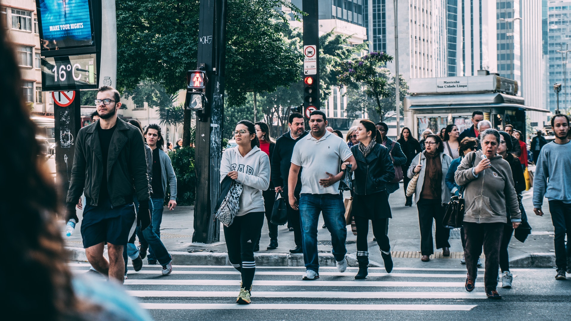 People crossing a busy downtown intersection with traffic lights and a digital display showing the temperature.