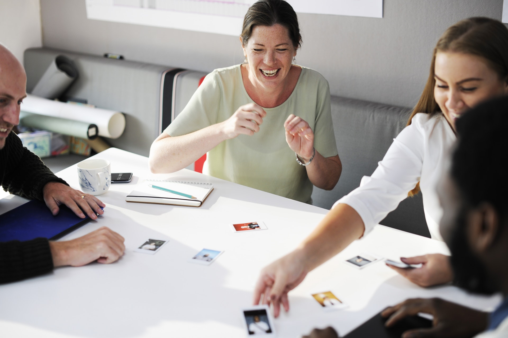 A group of colleagues laugh and engage in a discussion around a table scattered with photographs and various items.