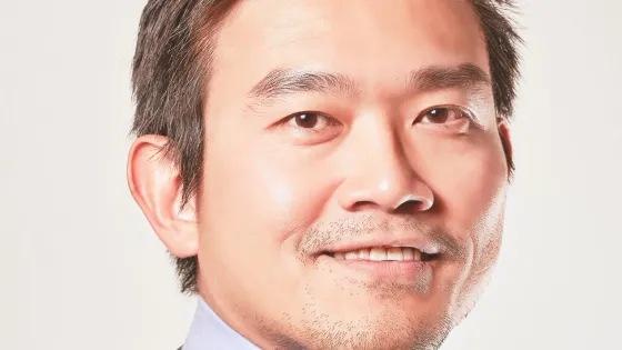 A professional headshot of a smiling Asian man wearing a suit and striped tie.