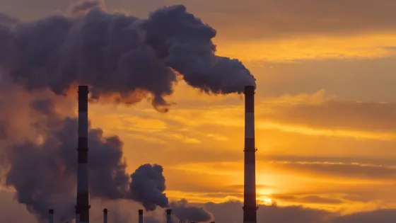 Sunset behind industrial area with stack emitting pollutants