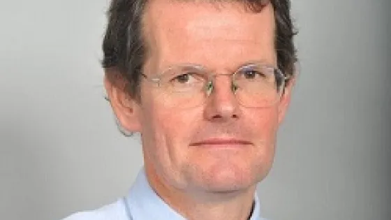 A portrait of a middle-aged man with glasses, wearing a blue shirt and a striped tie.