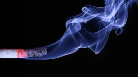 A lit cigarette with smoke swirling against a black background.
