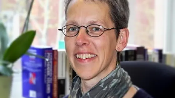 A woman with short hair and glasses smiling at the camera in an office setting.