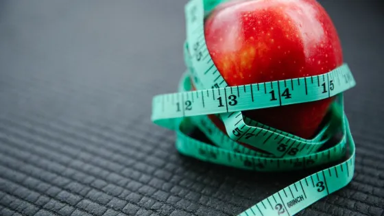 A red apple tightly wrapped with a green measuring tape on a textured dark background.
