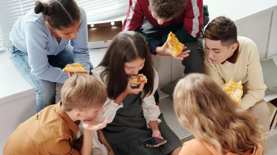 A group of teenagers enjoy eating pizza together in a casual, home setting.
