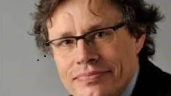 A portrait of a middle-aged man wearing glasses and a brown jacket, with a slight smile.