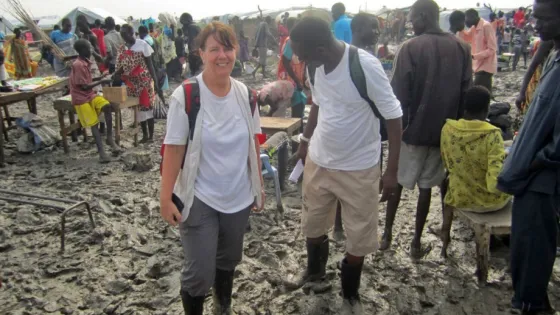 A woman and man walking through a bustling outdoor market with muddy ground.