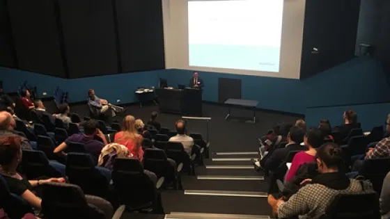 Audience attending a presentation in a modern lecture hall with a speaker at the podium.