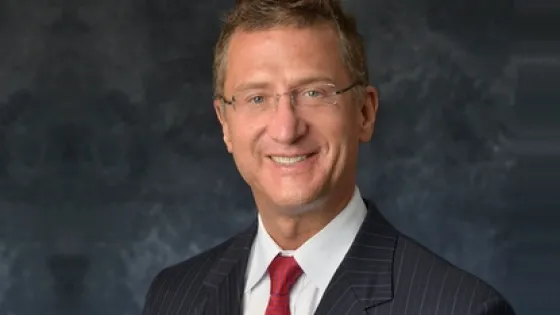 A professional portrait of a smiling man wearing a pinstripe suit and red tie.