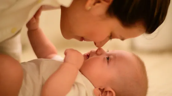 A woman gently touching noses with a smiling baby lying on a soft surface.