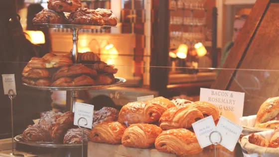 A display of various croissants and pastries in a warmly lit bakery.