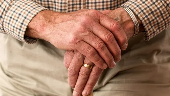 An elderly person's hands clasped over a walking stick.