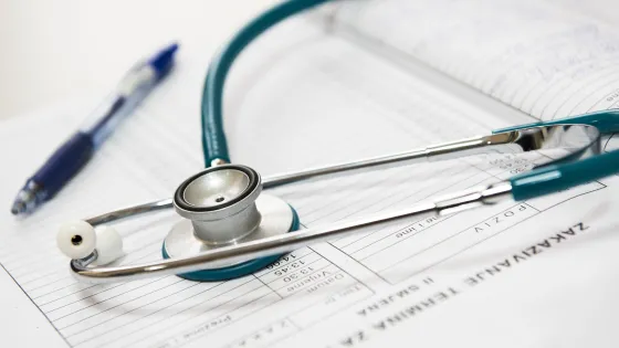A stethoscope and a pen lying on an open medical chart, indicating a clinical setting.