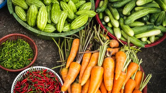 Various fresh vegetables including carrots, cucumbers, and chili peppers displayed in baskets at a market.