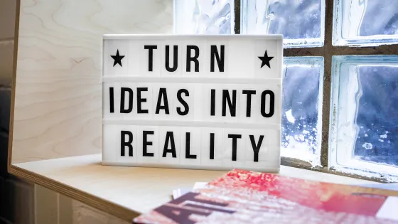 A lightbox sign reading "TURN IDEAS INTO REALITY" placed on a shelf by a window with translucent glass.