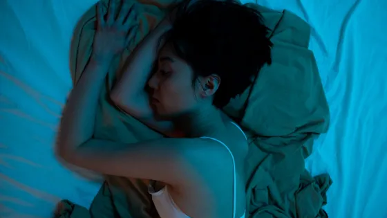 A woman sleeping in her bed under blue lighting.