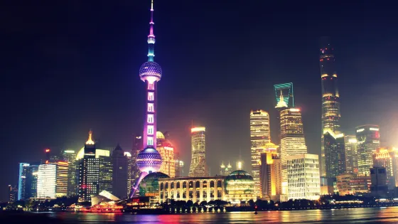 Night view of the illuminated Shanghai skyline featuring the Oriental Pearl Tower and modern high-rise buildings along the waterfront.