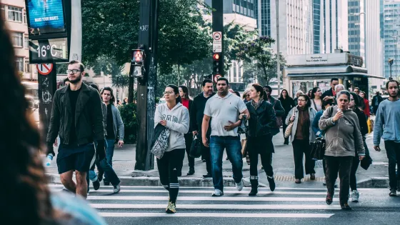 People crossing a busy downtown intersection with traffic lights and a digital display showing the temperature.