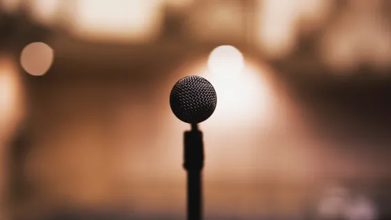 A microphone stands in focus against a softly blurred background with warm, glowing lights.
