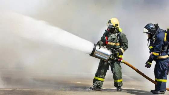 Firefighters in protective gear use a hose to spray a powerful jet of water during a training exercise.