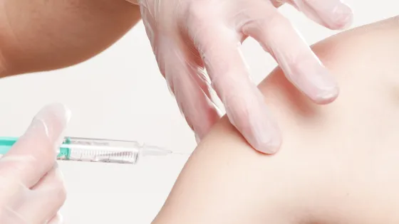 A person in gloves administering an injection into another person's upper arm.