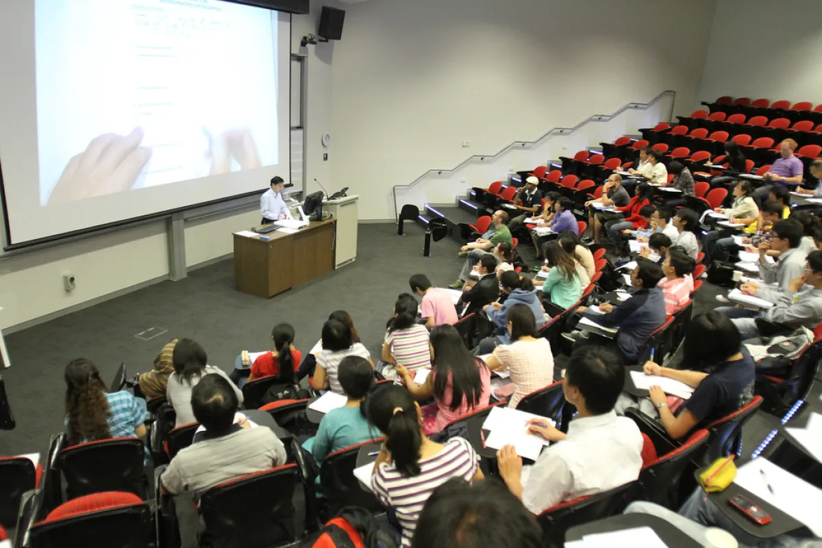 A lecturer speaks to a crowd of students in a large university auditorium.