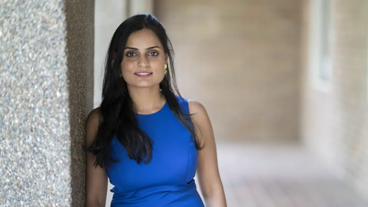 A woman in a blue dress stands smiling near a column in a hallway.