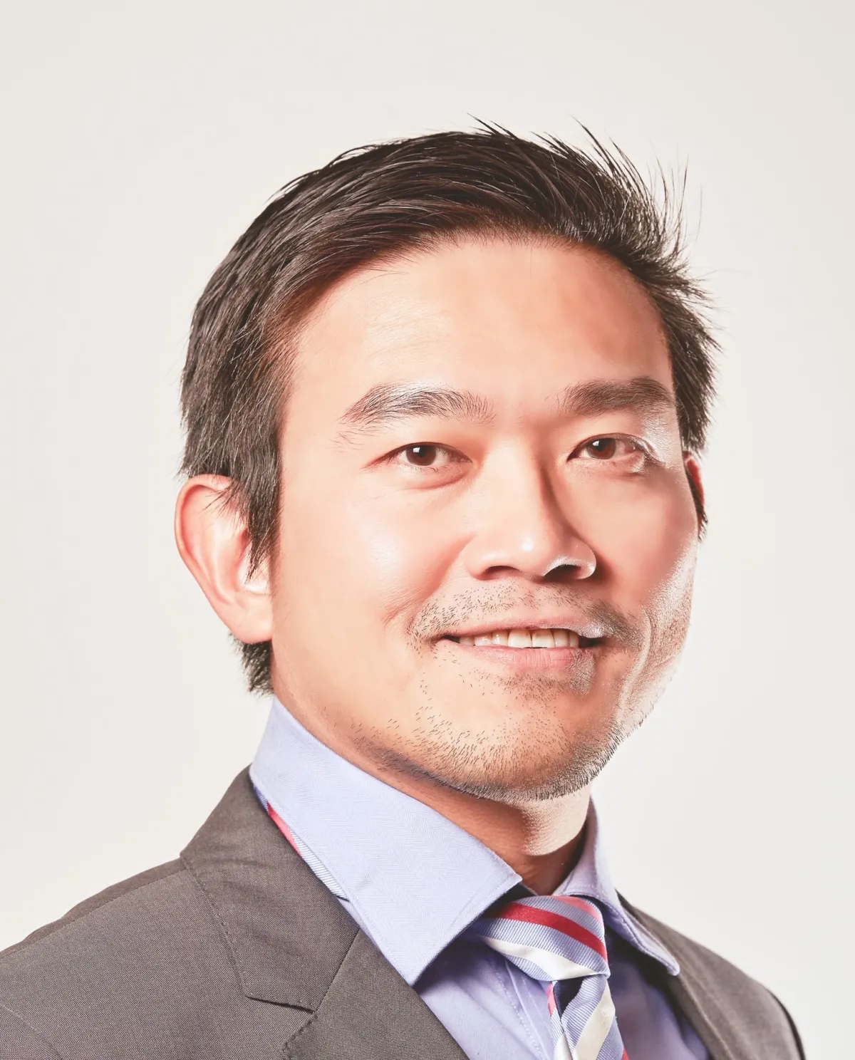 A professional headshot of a smiling Asian man wearing a suit and striped tie.