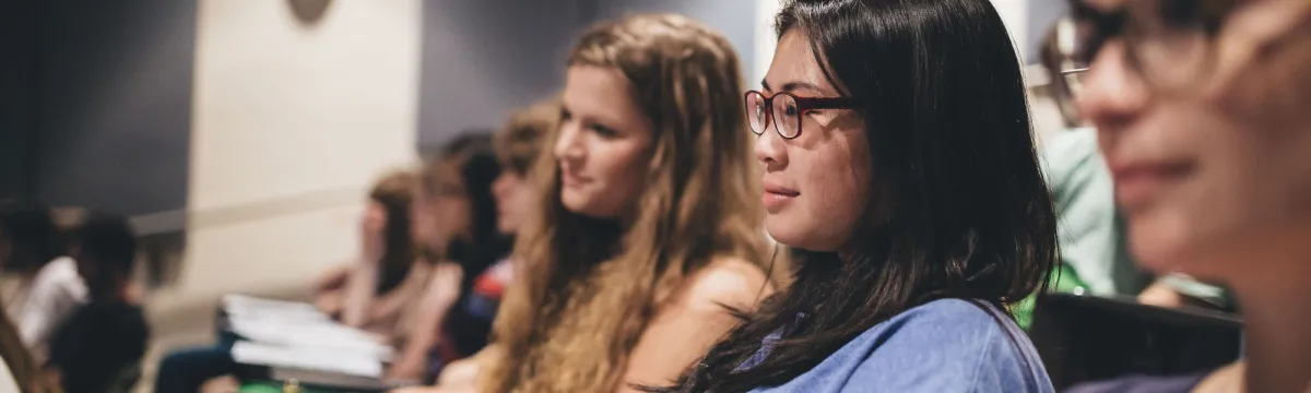 A row of female students listening attentively in a classroom.