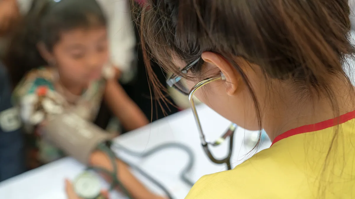 A young girl wearing glasses listens intently through a stethoscope in a medical learning environment.