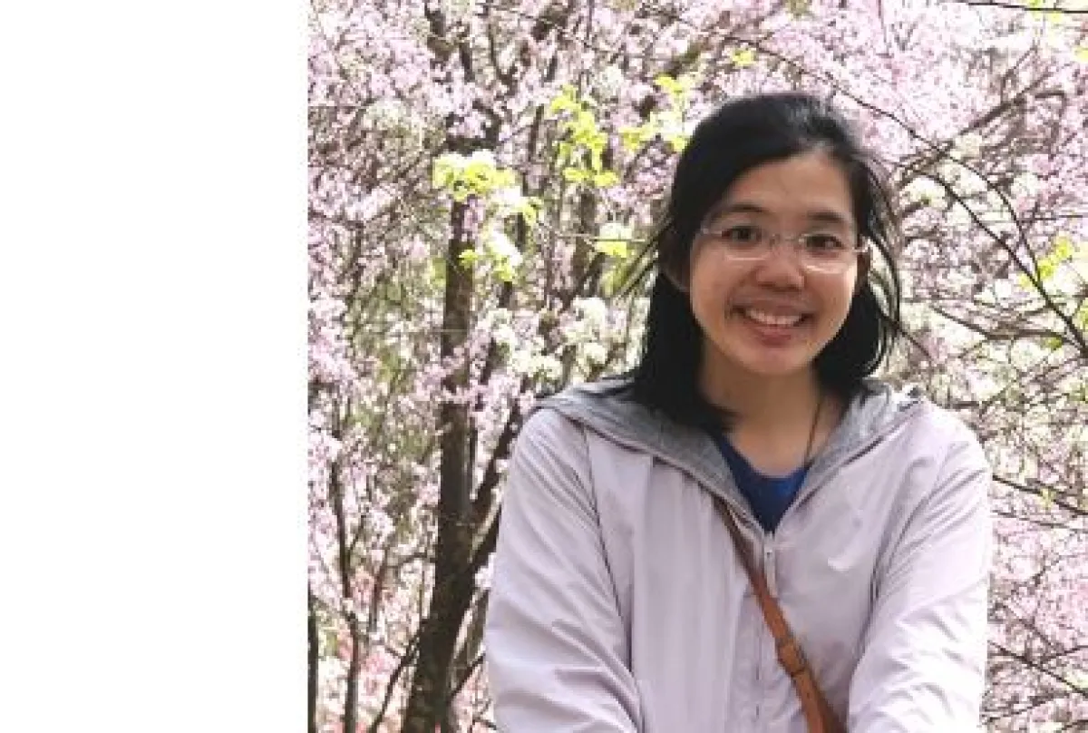 A woman smiling in front of cherry blossoms.
