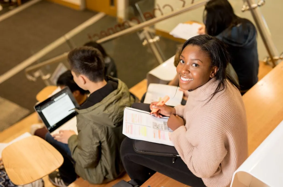 A young woman smiling at the camera while studying with classmates in a university classroom.