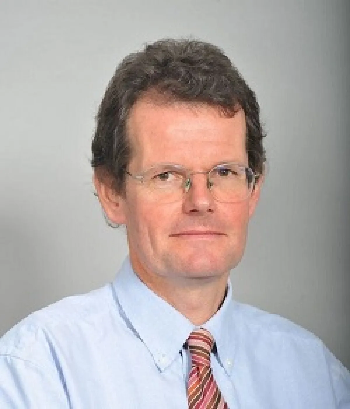 A portrait of a middle-aged man with glasses, wearing a blue shirt and a striped tie.