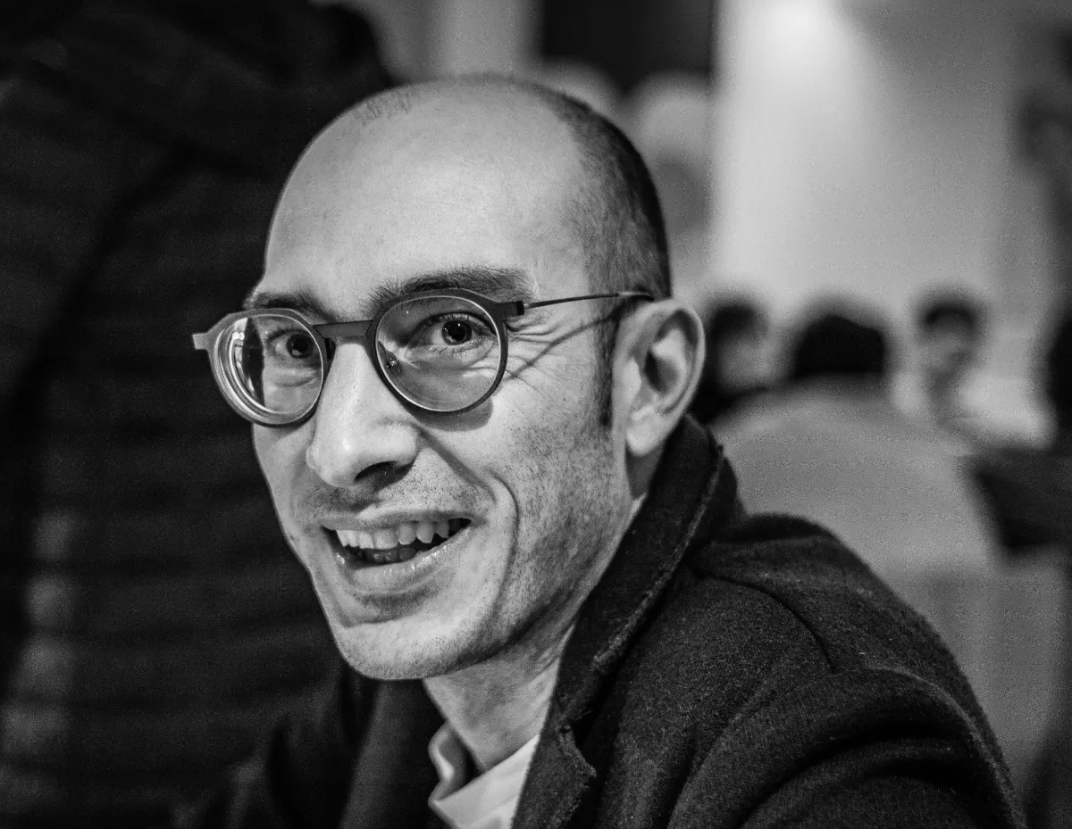A close-up black and white photo of a smiling man wearing round glasses.