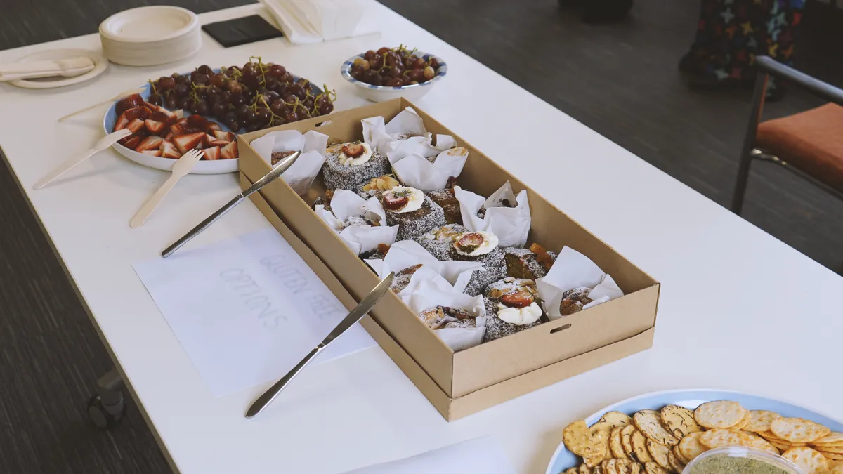 A buffet table with various snacks including bowls of grapes and strawberries, boxes of pastries, and plates with crackers and dips.